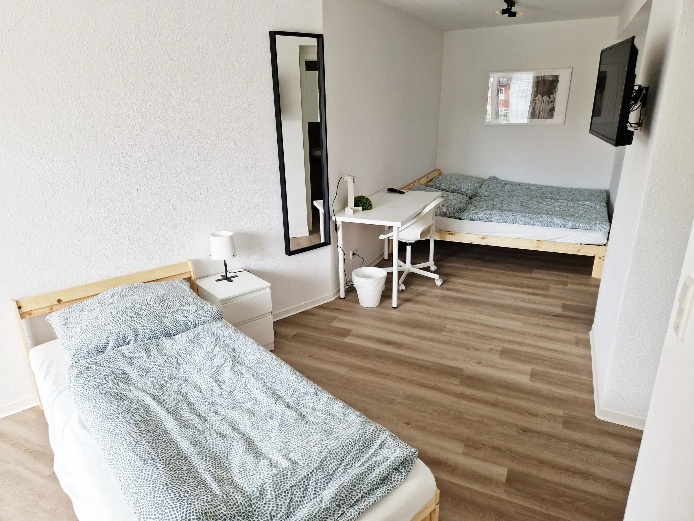 Einzelbett im Vordergrund des Dreibettzimmers, dahinter Schreibtisch und zweites Bett
