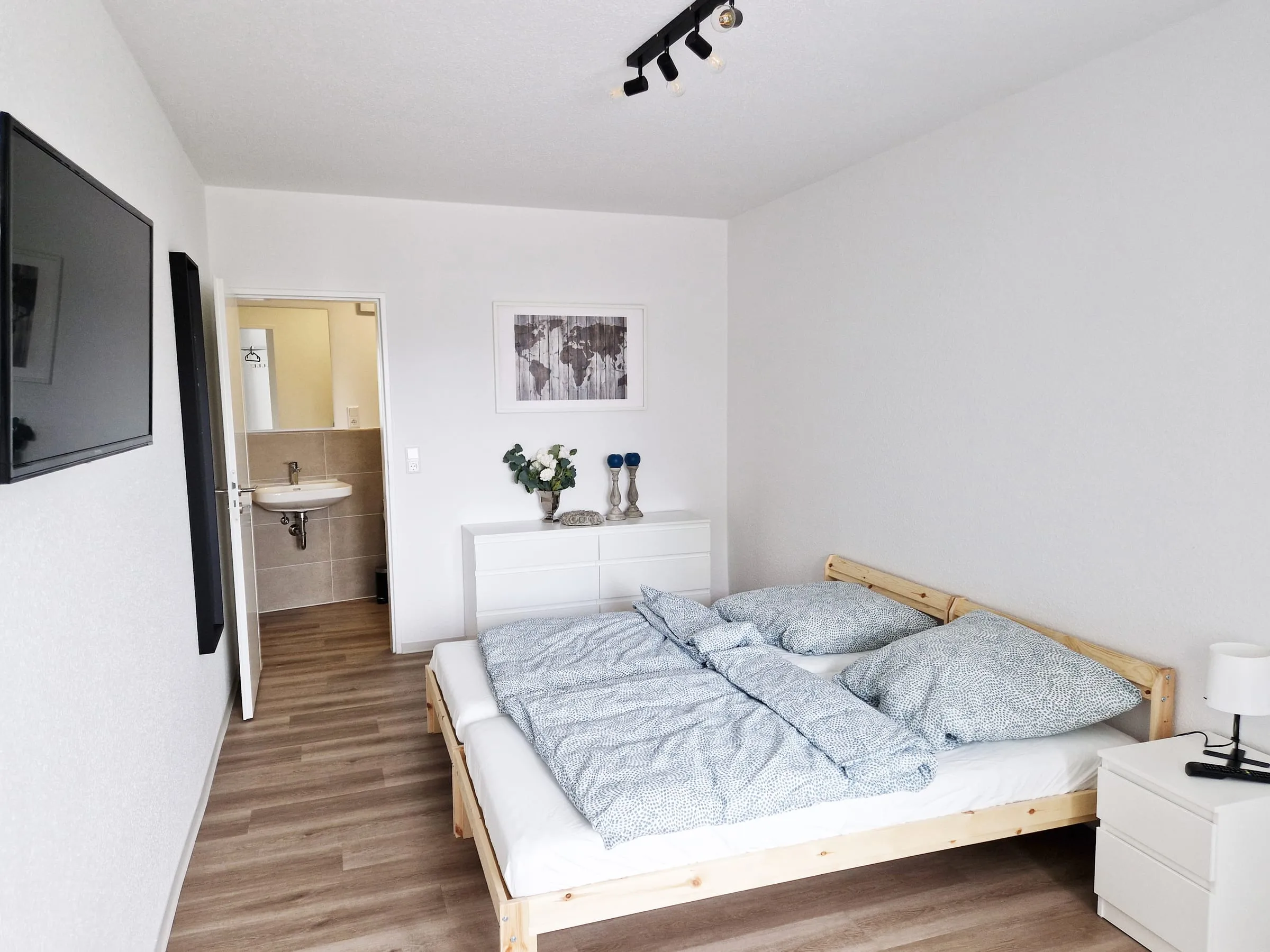 Doppelzimmer mit bezogenem Bett, Nachttischlampe und offener Tür zum eigenen Duschbad