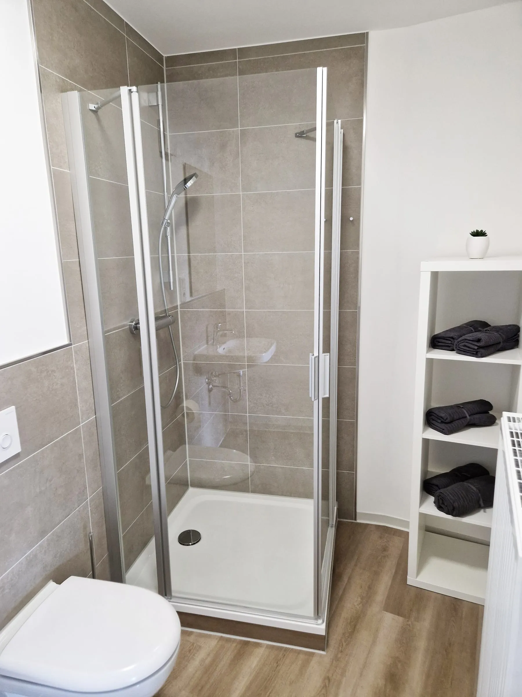 Duschkabine im Doppelzimmer, daneben ein Regal mit frischen Handtüchern